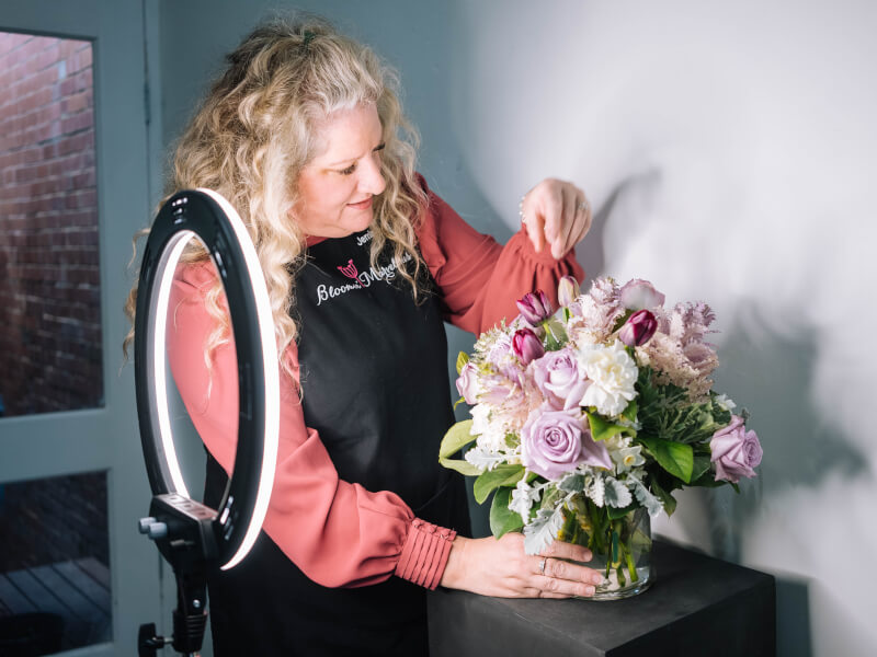 A person using a ring light to illuminate a floral arrangement